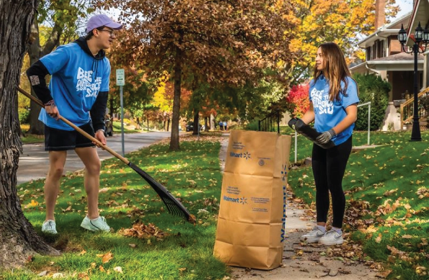 Two students raking in a neighbors yard