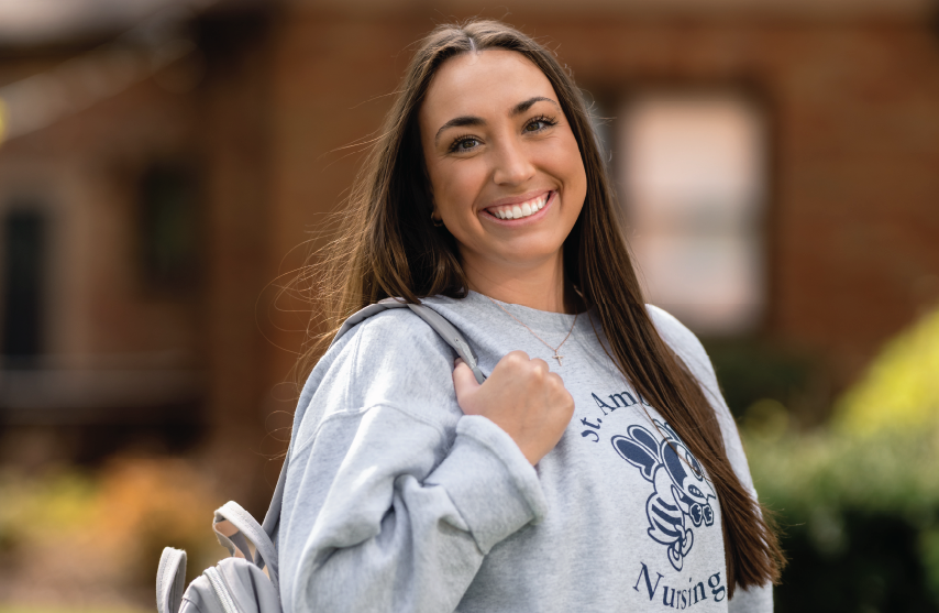 Student with backpack standing outdoors, smiling.