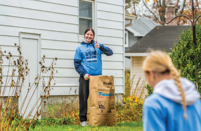 Student gives a thumbs-up while bagging leaves