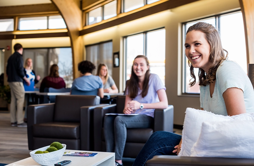 Two students sit in chairs next to windows while visiting St. Ambrose campus.