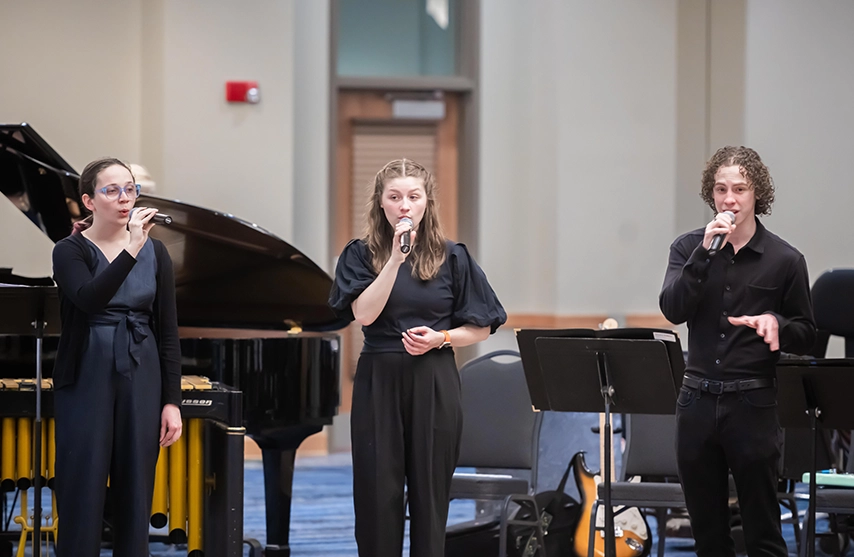 Three students sing into microphones during a performance.