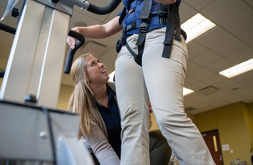 A young physical therapist assists a patient in walking on a treadmill.