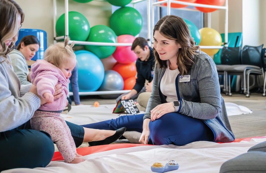 Two women sitting with a baby on the floor.