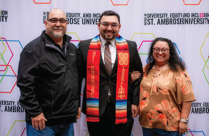 A student with a cultural stole posing with parental figures.