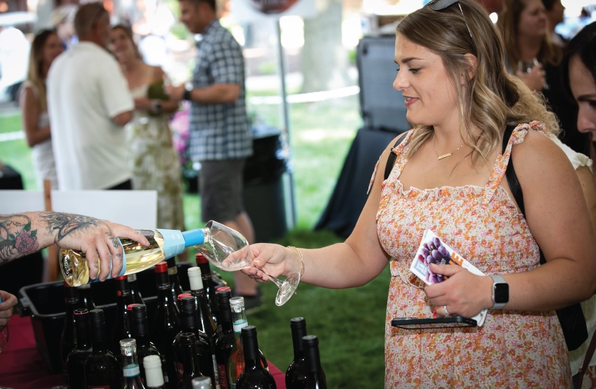 A woman getting wine at an outdoor alumni event.