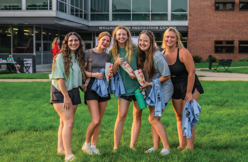 A group of students smiling outdoors in front of the Wellness and Recreation Center.