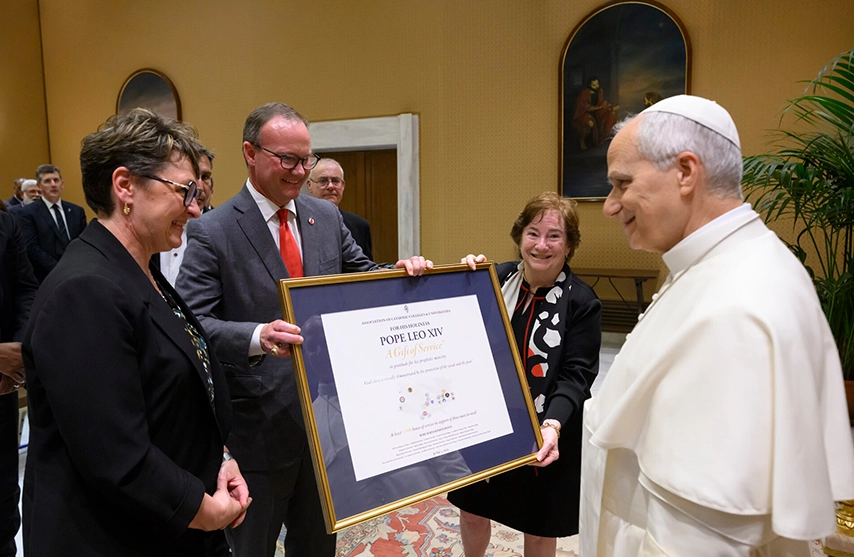 Amy Novak, EdD, president and CEO of St. Ambrose University and Mount Mercy University, presents a framed gift to Pope Leo XIV, alongside other members of the ACCU.