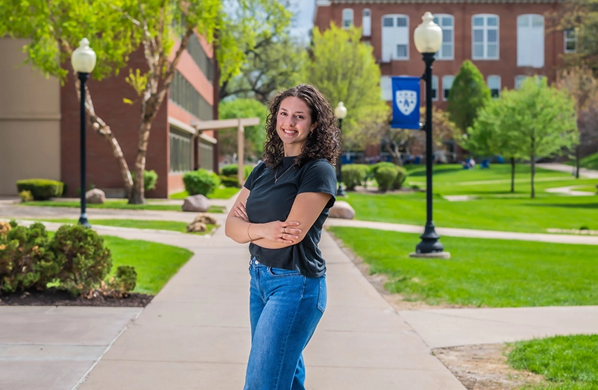 Delia Schwartz stands on St. Ambrose University's campus and smiles into the camera.