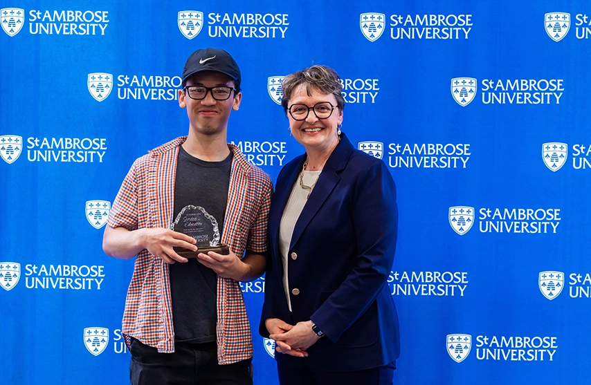 Presidential Award for Staff Excellence Award winner Nick Nguyen smiles as he stands next to President Amy Novak, EdD, and hold his trophy.