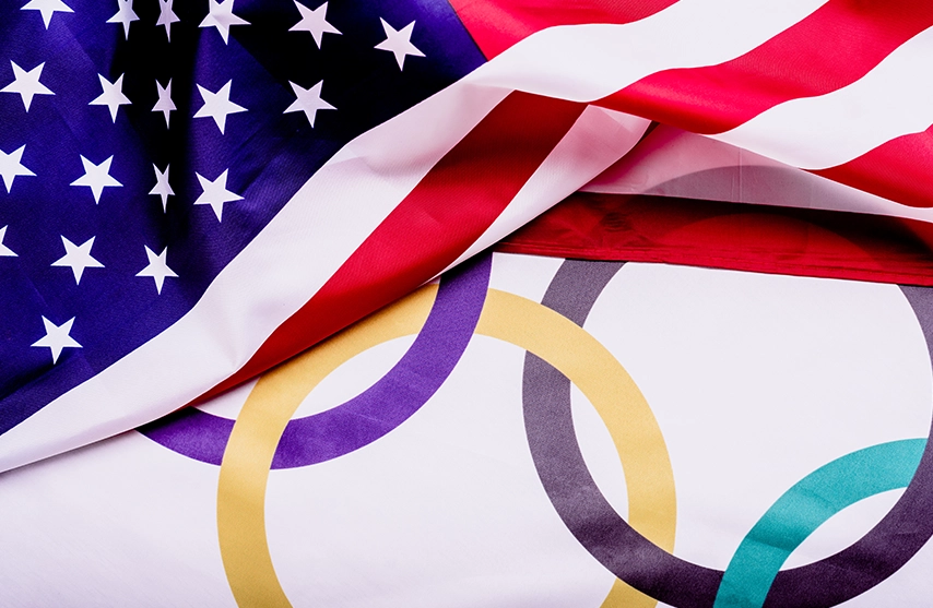 The flags of the United States of America and the flag of the Olympic games lay on top of one another.