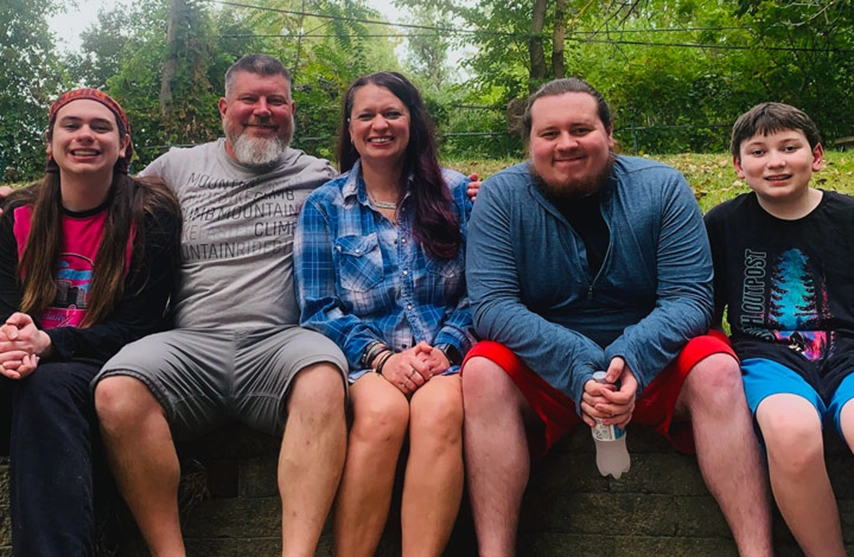 Nichole Plague sits next to her husband and 3 children as they all smile at the camera.