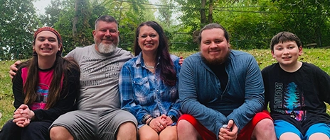 Nichole Plaggue sits next to her husband and 3 children and all smile at the camera.