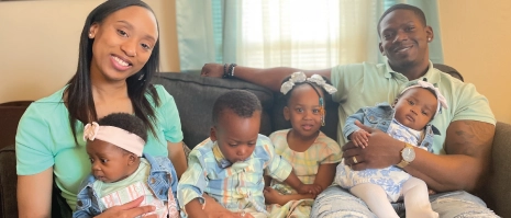 A man and a Woman sitting on a couch with 4 young children.