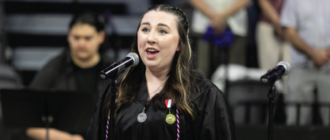 Student in graduation gown singing at commencement event.