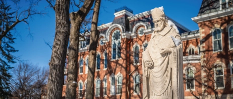 A stone statue of Saint Ambrose of Milan outside in the snow.