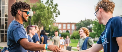 Students shaking hands outside at a campus event.