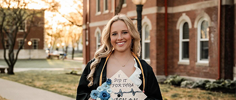Abby Messina holds up a decorated graduation cap and smiles at the camera.
