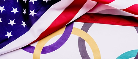 The flags of the United States of America and the flag of the Olympic games lay on top of one another.