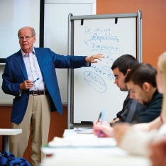 A man in a suit delivering a lecture to a group of students.