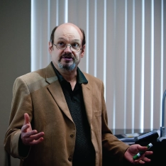 A man in a suit standing in front of a projector screen, delivering a presentation to an audience.