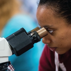 A woman examining a specimen under a microscope.