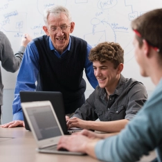 A professor helping students at a computer in a classroom.