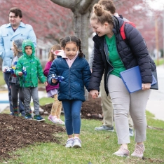 A woman and elementary student walking down a sidewalk outside their school.