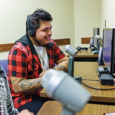 Two students wearing headphones observing a social work exercise with microphones and computers.