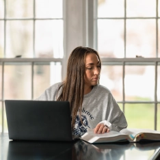 Student checking notes as she uses a laptop.