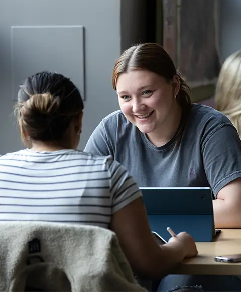 Two women sitting at a table with laptops, engaged in discussion.