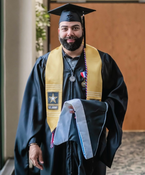 U.S. Army veteran wearing commencement gown and cap at graduation ceremony.