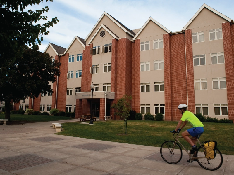 A cyclist riding on a path in front of a dorm.