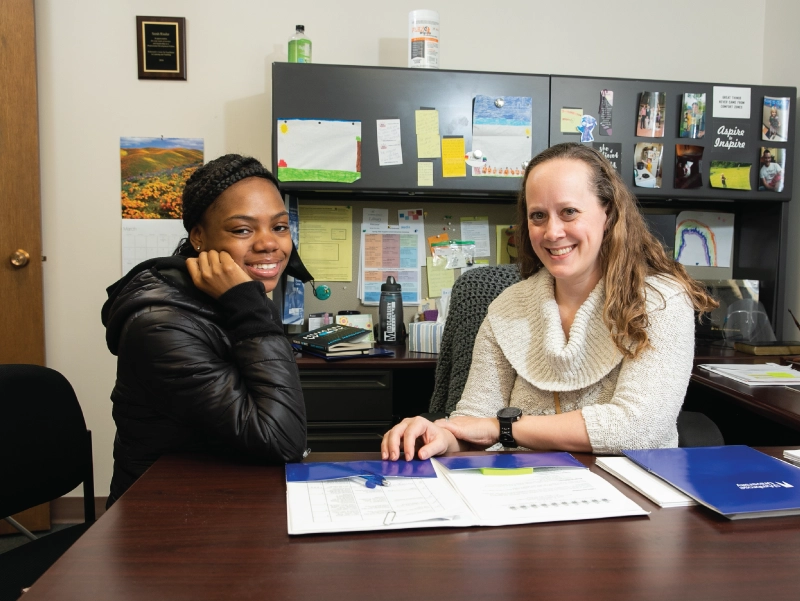 Two women sitting at a desk, looking over a folder together at Student Support.