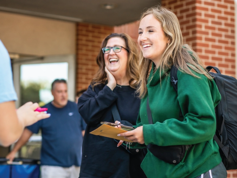 Student smiling with a parental figure outside