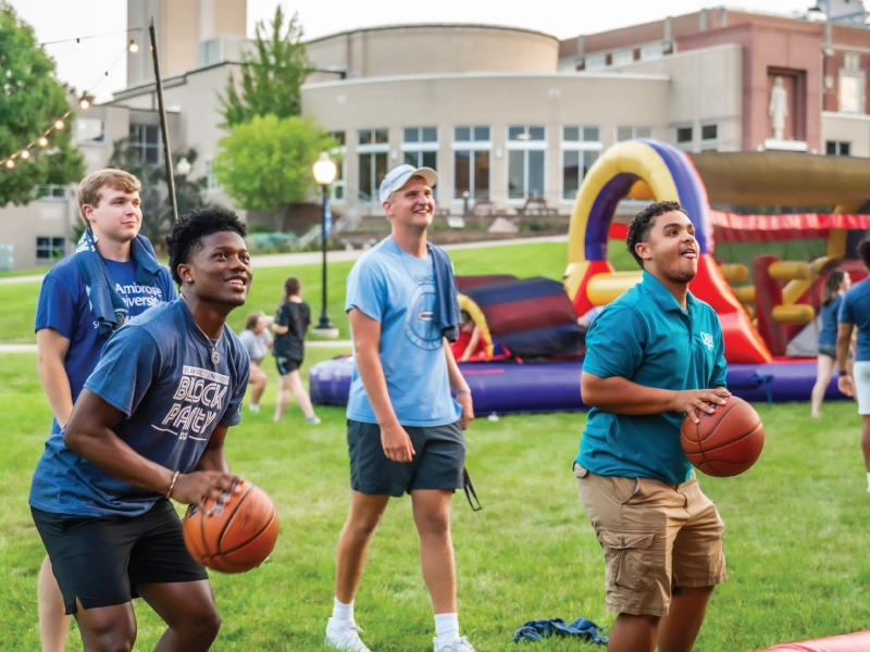 Two students shooting basketballs outside at an evening event.