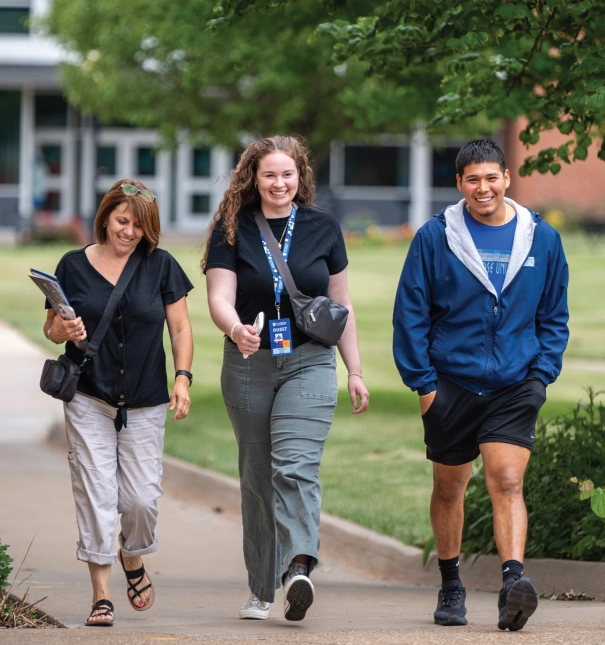 Three individuals walking across campus on a tour.