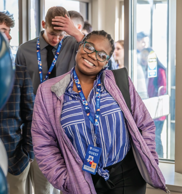 One female student walking into an event indoors, smiling.