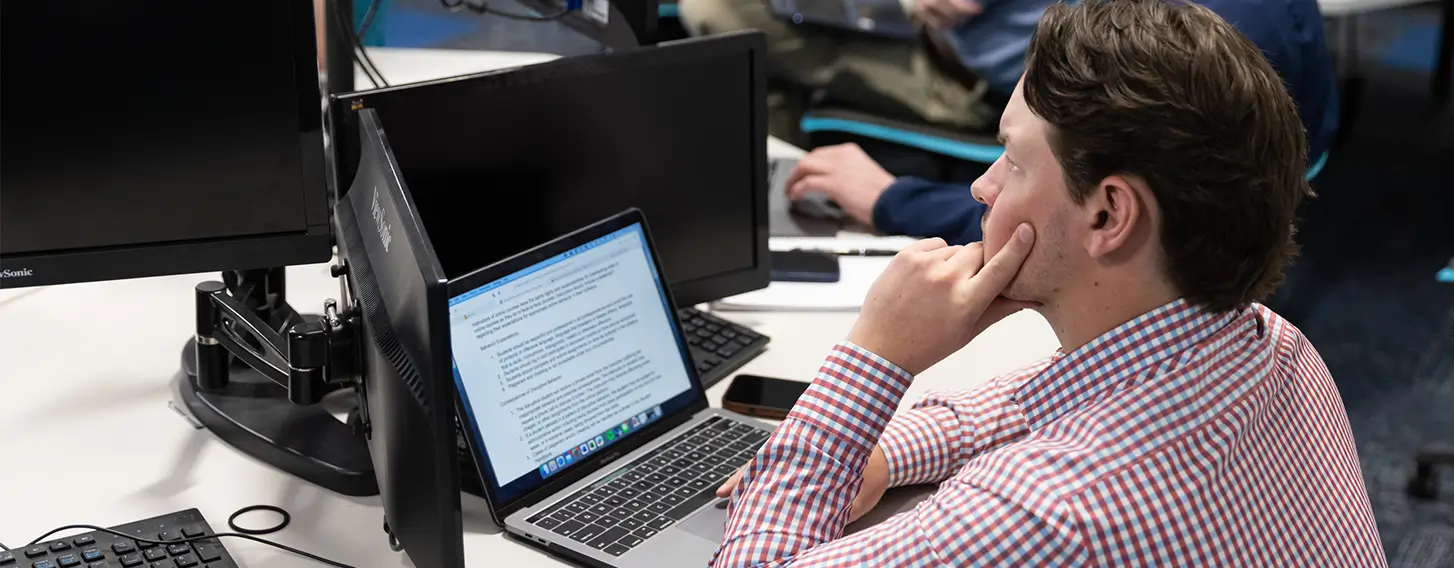 A group of individuals working at desks with computers, engaged in various tasks.