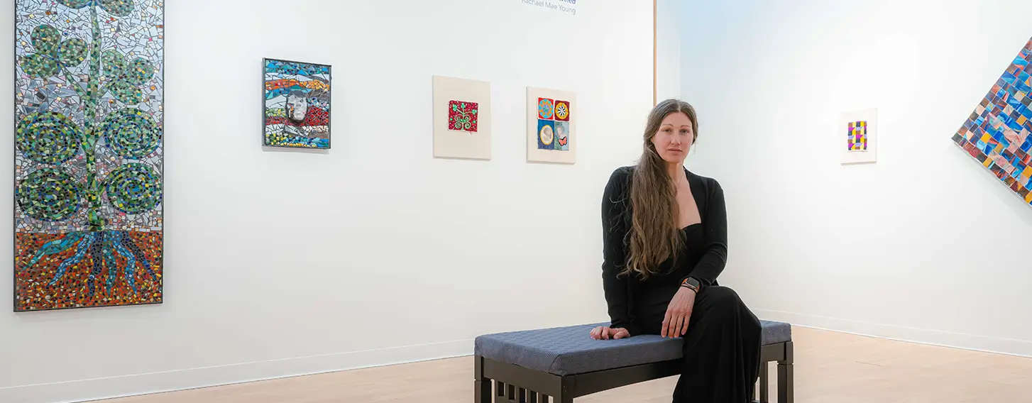 An art student sitting on a bench in a gallery. The exibit around her features her artwork.