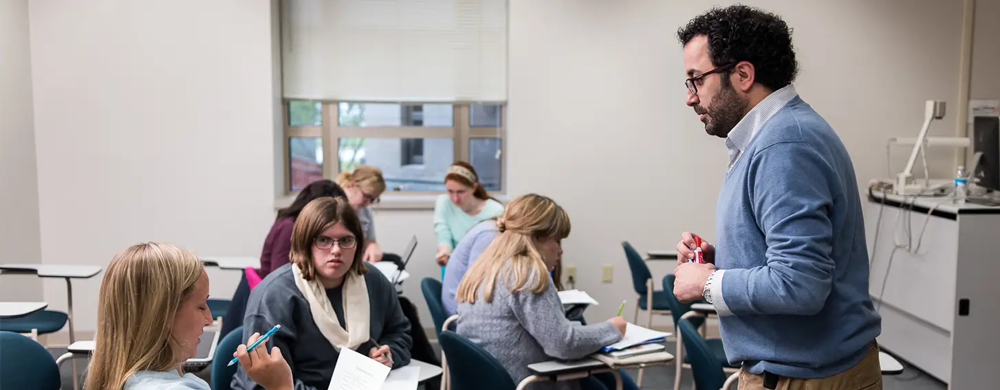 A man standing in front of a classroom full of students, giving a lecture.