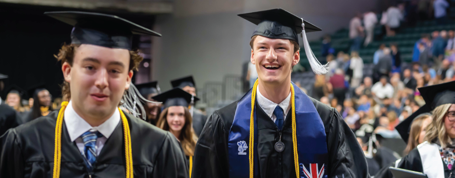 Bachelor degree graduate walking during commencement, smiling.