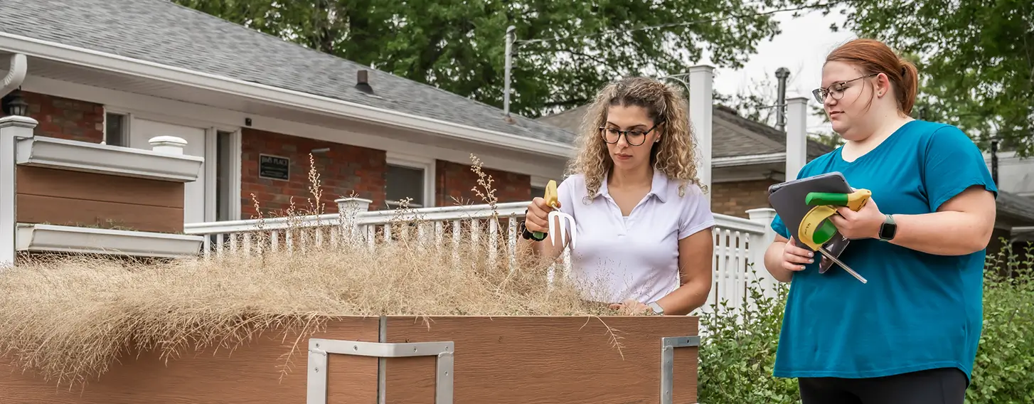 Two women working conducting an assessment outdoors next to a raised planter.