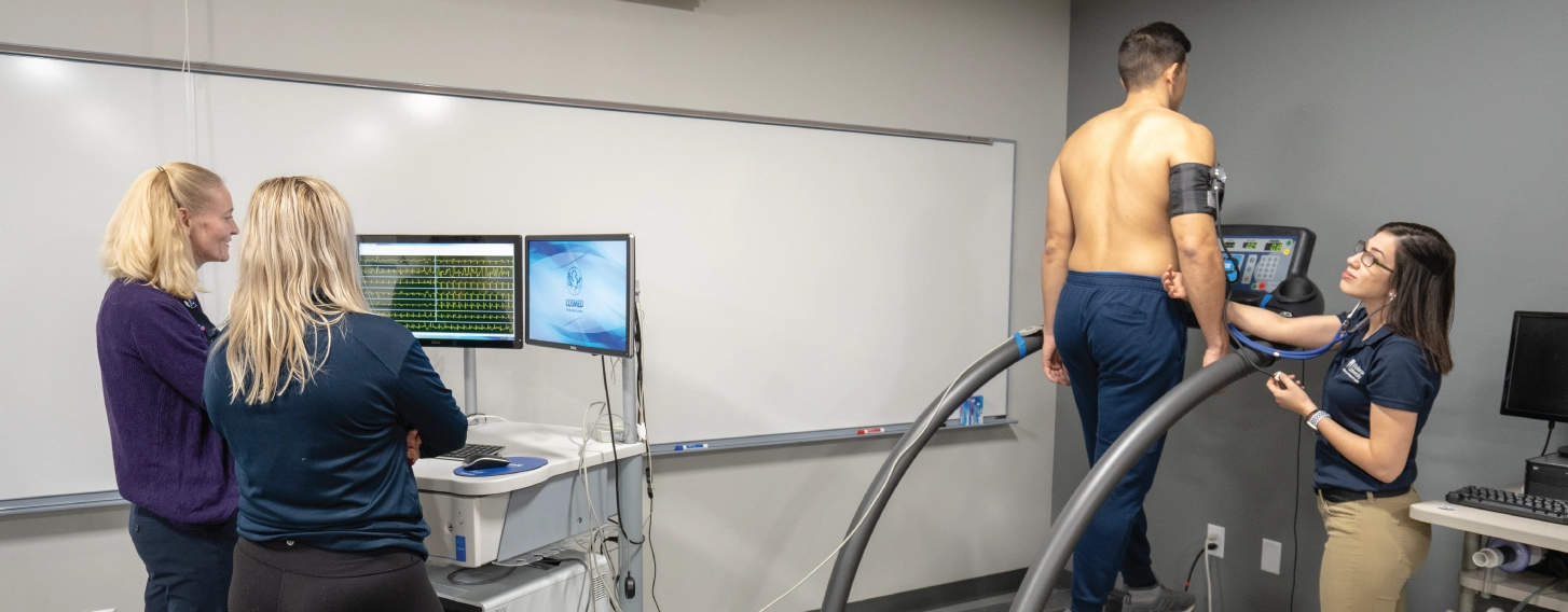 A man exercising on a treadmill while three women monitor his responses.