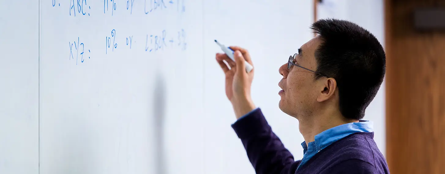 A professor writing on a whiteboard in a math course.