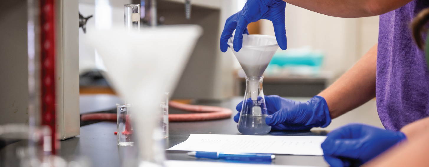 Gloved hands conducting chemistry experiment.