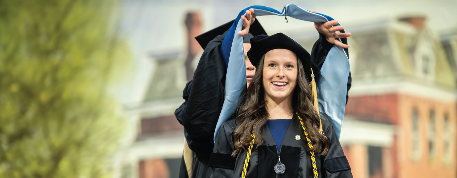 Doctoral graduate receiving hood during commencement ceremony.