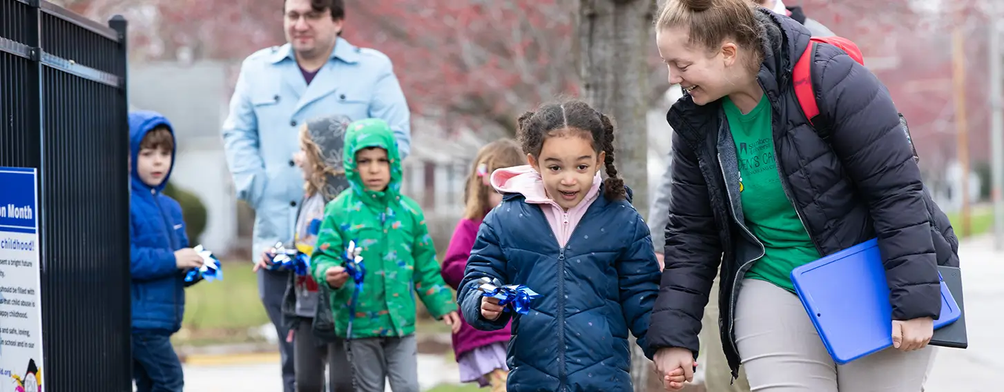 A woman and elementary student walking down a sidewalk outside their school.