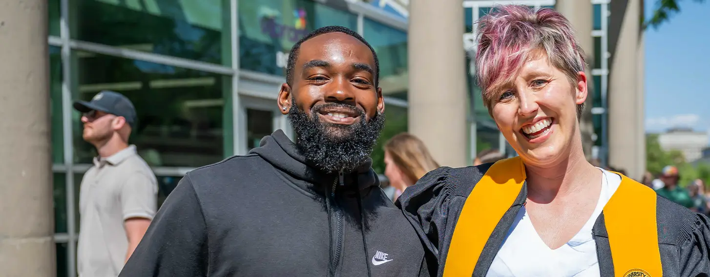 A faculty member and a student posing together outside at commencement