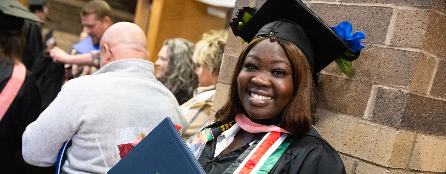 A graduate smiling, wearing a South Sudan flag stole at commencement