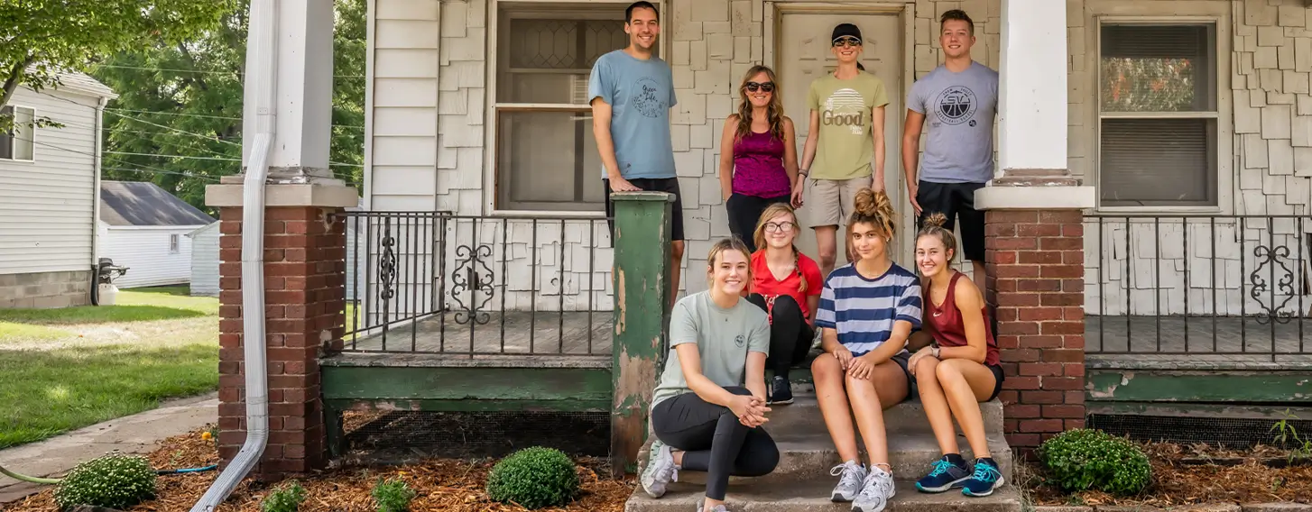 A group of people posing in front of a white campus house.